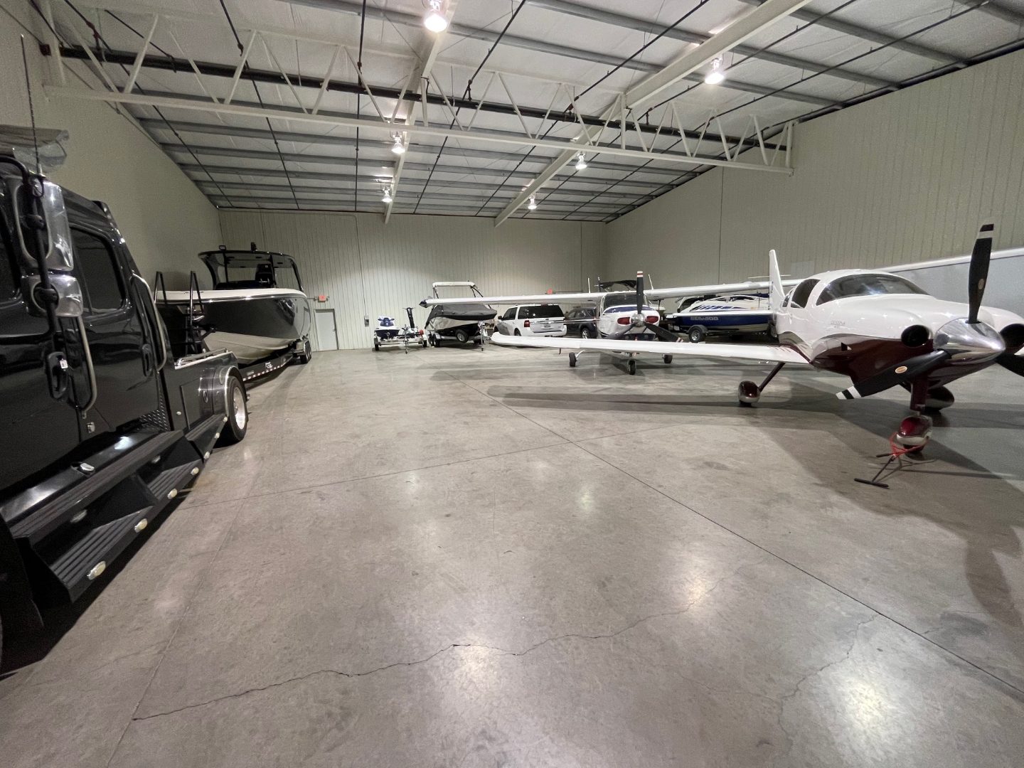 Wide-angle hangar interior with a truck, boats, and multiple aircraft